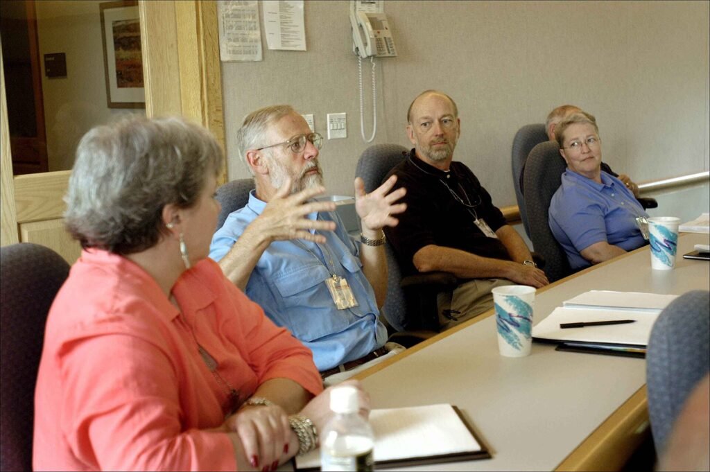 People seated at table participating in group discussion during meeting, representing a conversation about treatment costs